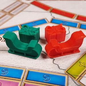May include: Four game pieces for a board game. Two are red sleighs and two are green sleighs with presents on top.