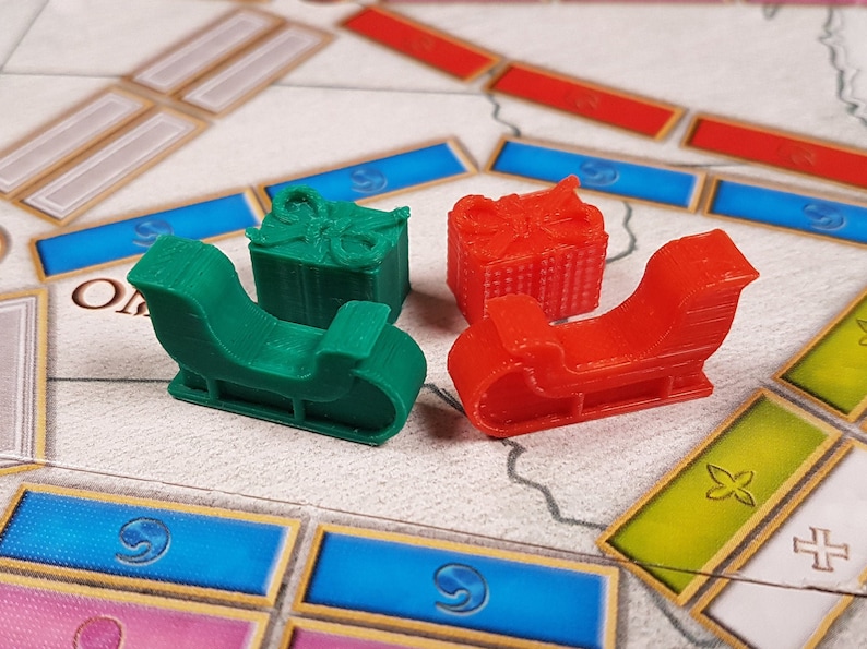 May include: Four game pieces for a board game. Two are red sleighs and two are green sleighs with presents on top.