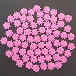 May include: A large group of pink plastic flower-shaped buttons. The buttons are arranged in a circular pattern.