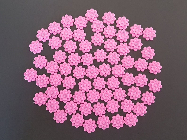 May include: A large group of pink plastic flower-shaped buttons. The buttons are arranged in a circular pattern.