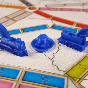 May include: Three blue plastic game pieces: a train with a dragon wing, a train with a chimney, and a round hat with a brim.