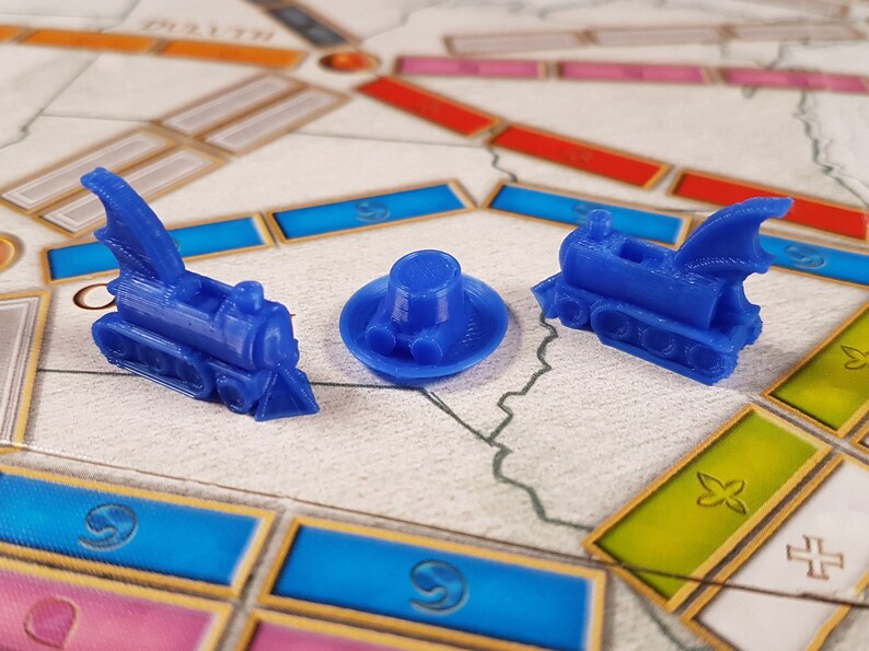 May include: Three blue plastic game pieces: a train with a dragon wing, a train with a chimney, and a round hat with a brim.