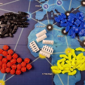 May include: A collection of game pieces for a board game. The pieces are in different colours, including black, white, red, yellow, and blue. The pieces are arranged in groups on a blue and white game board.