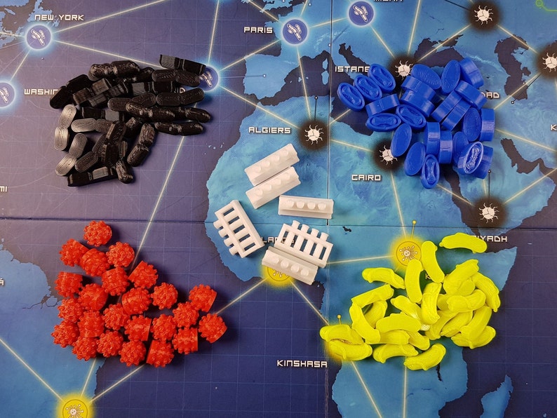 May include: A collection of game pieces for a board game. The pieces are in different colours, including black, white, red, yellow, and blue. The pieces are arranged in groups on a blue and white game board.