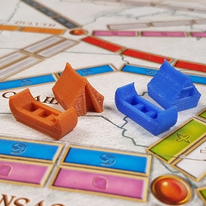 May include: Two miniature wooden houses, one blue and one brown, are placed on a board game with a map of the United States. The houses are made of wood and have a simple design.