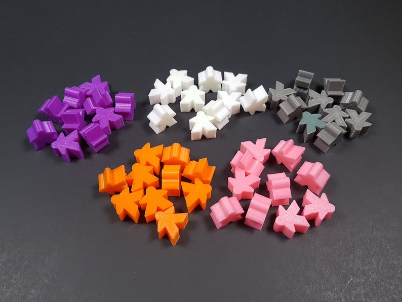 May include: A collection of 5 different colored plastic game pieces. The pieces are shaped like people and are in the colors purple, white, gray, orange, and pink.