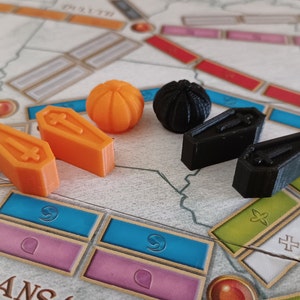 May include: A set of game pieces for a board game. The pieces include two orange coffins, two black coffins, a black sphere, and an orange sphere.
