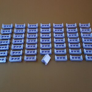 May include: A collection of 48 small, light purple plastic pieces arranged in a grid pattern. Each piece has a rectangular shape with three evenly spaced holes.