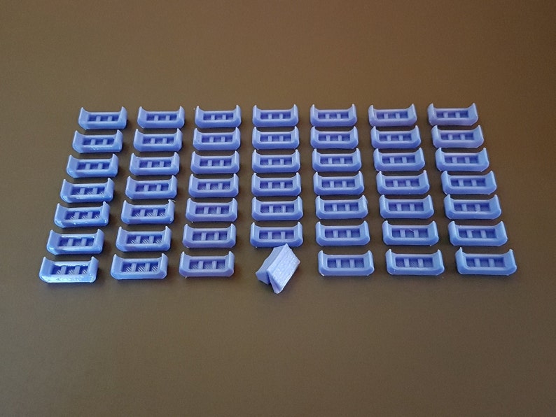 May include: A collection of 48 small, light purple plastic pieces arranged in a grid pattern. Each piece has a rectangular shape with three evenly spaced holes.