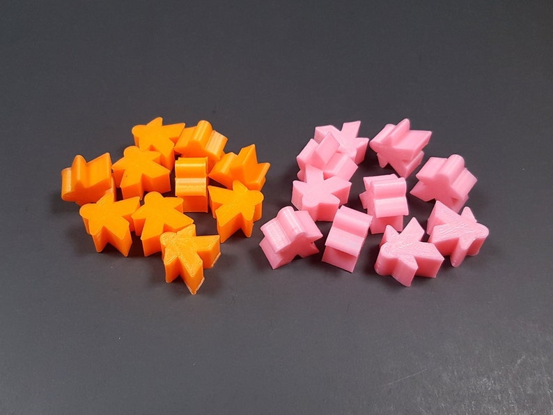 May include: A group of 12 orange and 10 pink plastic game pieces. The pieces are shaped like people.