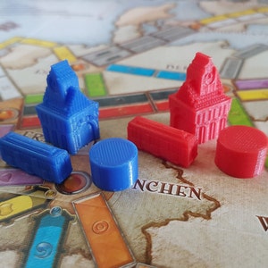 May include: A set of game pieces for a board game. The pieces are made of plastic and come in two colors: blue and red. There are two tall buildings, two short buildings, and two round pieces.