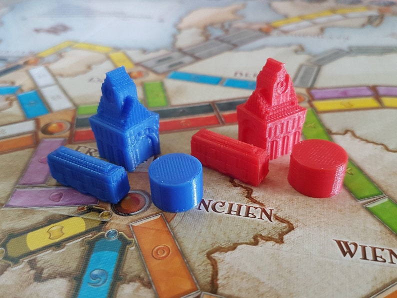 May include: A set of game pieces for a board game. The pieces are made of plastic and come in two colors: blue and red. There are two tall buildings, two short buildings, and two round pieces.