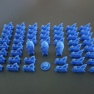 May include: A collection of 3D printed blue rocket ship figurines. There are 37 rocket ships, 3 larger rocket ships, and a small blue disc.