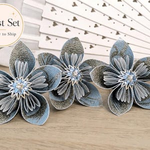May include: A set of three dimensional paper flowers in shades of light blue and metallic gold. Each flower features layered petals with a central cluster of light blue and clear rhinestones. The text "Last Set Ready to Ship" is visible.