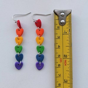 K&ouml;nnte beinhalten: Regenbogen-Herz-Ohrringe mit silbernen Haken. Die Ohrringe sind etwa 6 cm lang.