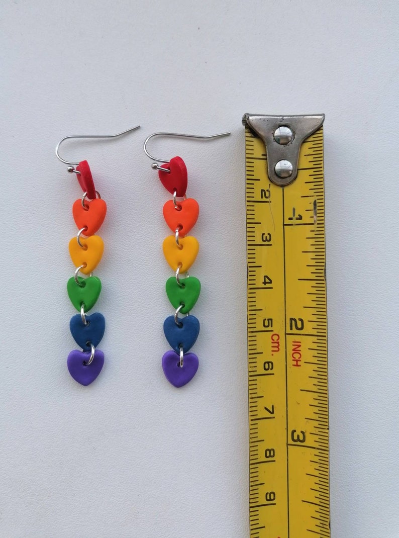 K&ouml;nnte beinhalten: Regenbogen-Herz-Ohrringe mit silbernen Haken. Die Ohrringe sind etwa 6 cm lang.
