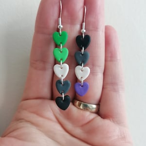 Könnte beinhalten: Ein Paar Ohrringe mit einem silbernen Haken und fünf herzförmigen Perlen. Die Perlen sind grün, weiß, grau, schwarz und lila.