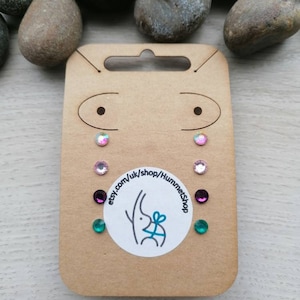 May include: A set of six pairs of stud earrings on a brown card with a white sticker featuring a rabbit with a gift. The earrings are in pink, purple, and green.
