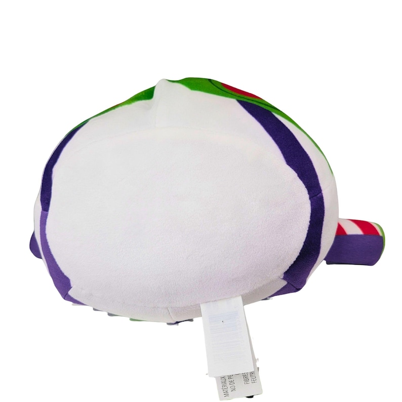 May include: A plush toy shaped like Buzz Lightyear from Toy Story. The toy is primarily white with green, purple, red, and black accents. It has a rounded shape with a small tag attached. The toy is made of a soft, plush material.
