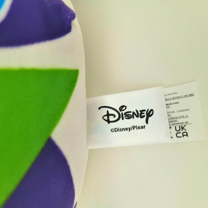 May include: A white tag with the Disney logo and the text "&copy;Disney/Pixar" is attached to a plush toy. The toy has a green, purple, and white pattern. Additional text is visible on the tag.