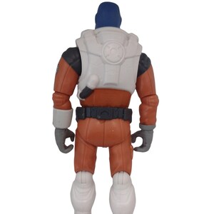 May include: A toy action figure of a space explorer, viewed from the back. The figure is wearing an orange jumpsuit, a white vest with a circular design, and a blue helmet. The gloves and boots are gray and white.