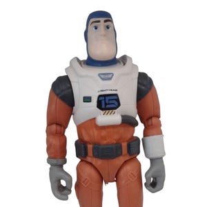 May include: A Buzz Lightyear action figure in a space suit. The figure has a blue head and a white and orange spacesuit with the number 15 on the chest. The figure is wearing gray gloves.