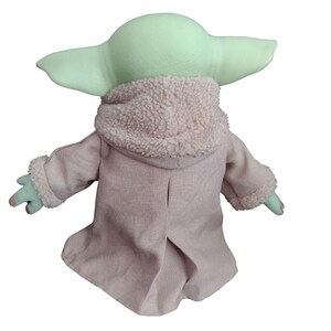 Op de afbeelding: Een groen pluche speelgoed met grote oren dat een bruine jas draagt met een witte bontkraag. Het speelgoed is een populair personage uit de Star Wars-franchise.