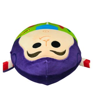 May include: A plush toy shaped like Buzz Lightyear from Toy Story. The toy has a purple head and a green and blue helmet. The face has black eyes and a stitched smile. The arms have red and white stripes.