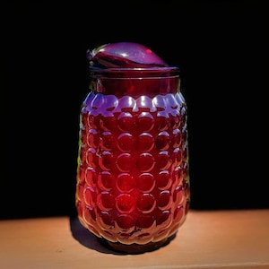 May include: A deep red glass pitcher with a textured, bubble-like surface. The pitcher has a lid and a spout.