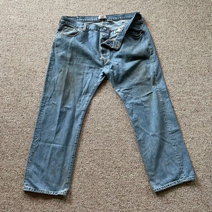 May include: A pair of light blue denim jeans with a button fly and a 501 label.