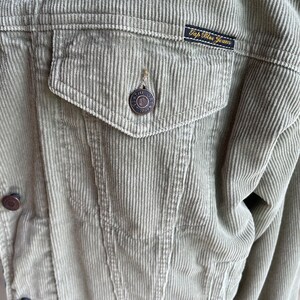 Op de afbeelding: Een lichtgroen corduroy jack met knoopsluiting en een patch op de zak met de tekst "Gap Blue Jeans".