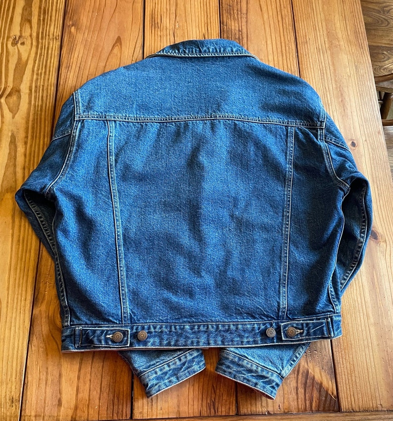 Op de afbeelding: Een blauwe denim jas met een klassiek ontwerp. De jas heeft een knoopsluiting, lange mouwen en twee zakken op de borst.