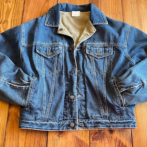 Op de afbeelding: Een blauwe denimjas met een corduroy kraag en knoopsluiting. De jas heeft twee voorzakken en twee borstzakken.