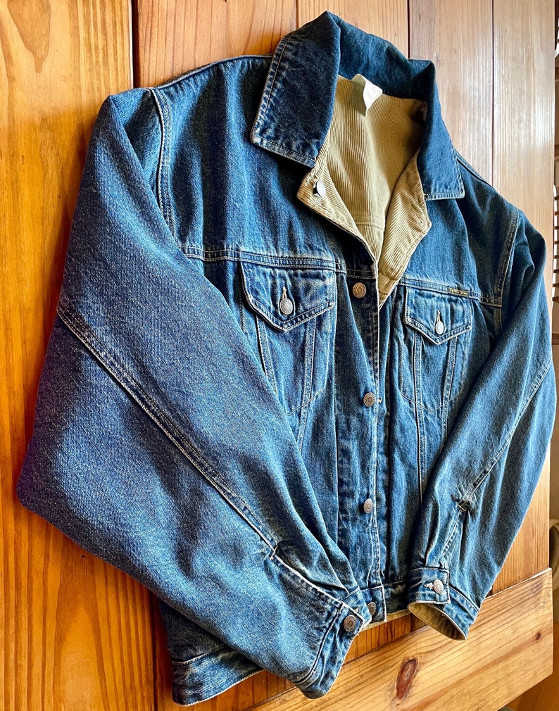 Op de afbeelding: Een blauwe denimjas met een corduroy voering. De jas heeft een knoopsluiting en twee voorzakken.