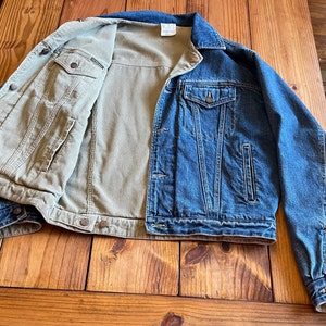 Op de afbeelding: Een spijkerjack met een corduroy voering. Het jack is blauw en de voering is beige. Het jack ligt plat op een houten oppervlak.