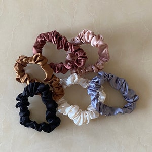 Op de afbeelding: Set van zeven kleurrijke scrunchies gemaakt van zijdeachtig materiaal. De scrunchies zijn in verschillende tinten bruin, roze, wit en grijs.