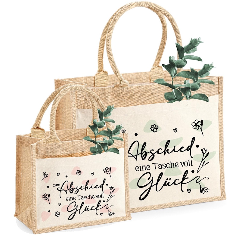 Pu&ograve; includere: Due borse tote in iuta beige con tasche bianche, con il testo tedesco "Abschied eine Tasche voll Gl&uuml;ck" in corsivo nero. Le borse hanno manici beige e sono decorate con rametti verdi e motivi floreali.