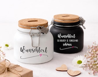 Könnte beinhalten: Zwei Keramikgläser mit Korkdeckeln und Metallbügelverschluss, eines in Weiß und eines in Schwarz. Das weiße Glas trägt den Text "Wunschtext" mit einem kleinen rosa Herz. Das schwarze Glas zeigt "Wunschtext SEI KREATIV & SCHREIB WAS schönes".