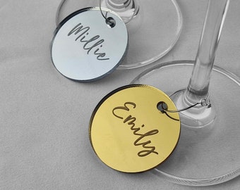 May include: Two round acrylic wine glass charms, one silver with the name Millie and one gold with the name Emily.
