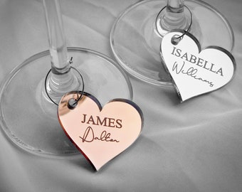 May include: Two heart-shaped wine glass charms with names engraved on them. The charm on the left is rose gold and says "JAMES Dalton". The charm on the right is silver and says "ISABELLA Williams".