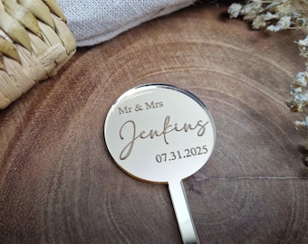 May include: Gold mirror acrylic wedding cake topper with the text "Mr & Mrs Jenkins 07.31.2025".