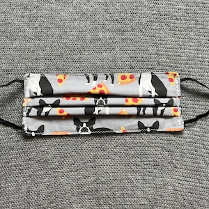 May include: A gray fabric face mask with a repeating pattern of black and white Boston Terriers eating pizza slices.