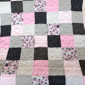 May include: A pink, black, and gray patchwork quilt with a sheep pattern. The quilt is made of squares of different fabrics and is quilted with a heart design.