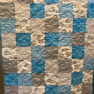 May include: A blue and gray baby quilt with a whale pattern. The quilt is made of squares with different whale designs.