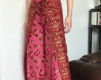 May include: Wide-leg pants in a vibrant pink and red floral pattern with gold accents. The pants feature a tie waist and a split at the hem. The fabric has a shiny appearance, suggesting a silk or satin material.