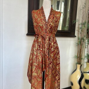 May include: A red and gold patterned sleeveless robe with a V-neck and a tie belt. The robe is made of a silky fabric and has a geometric design.