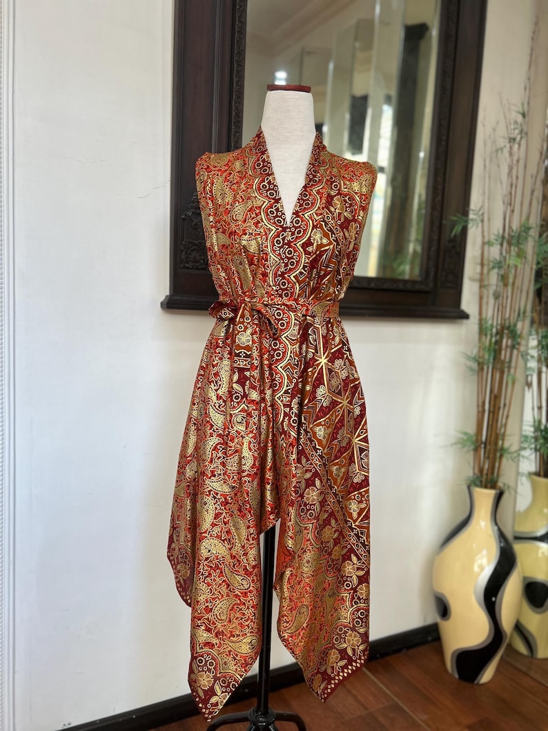 May include: A red and gold patterned sleeveless robe with a V-neck and a tie belt. The robe is made of a silky fabric and has a geometric design.