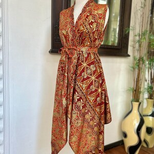 May include: A sleeveless red and gold patterned dress with a V-neck and a tie belt. The dress has a geometric pattern and a flowing, asymmetrical hem.