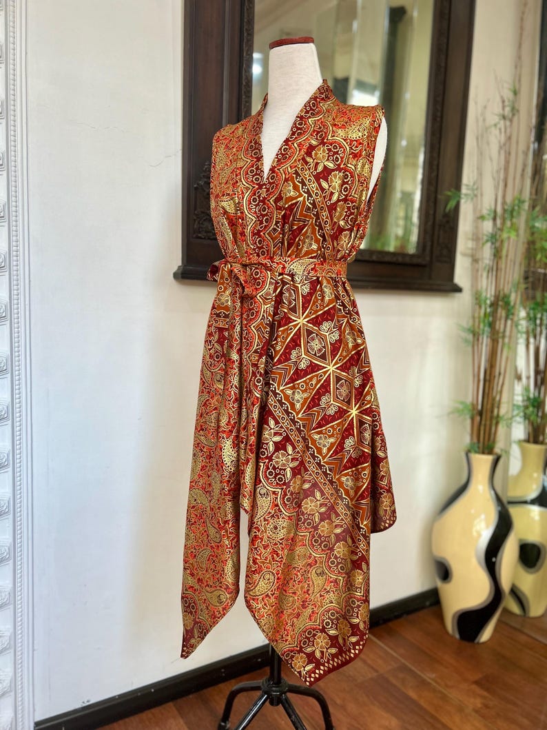 May include: A sleeveless red and gold patterned dress with a V-neck and a tie belt. The dress has a geometric pattern and a flowing, asymmetrical hem.
