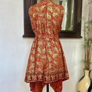 May include: A sleeveless red and gold paisley print dress with a high neckline and a high-low hemline.